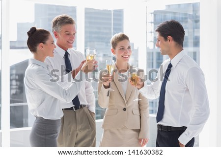 Smiling team of business people clinking their flutes of champagne in a bright office