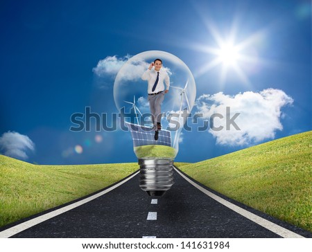 Businessman into light bulb with wind turbines and solar panels running on a road with bright blue sky on the background