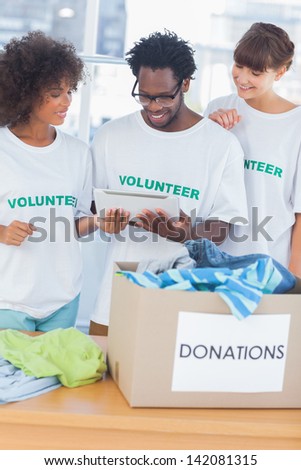 Cheerful volunteers looking at a tablet pc in front of a donations box