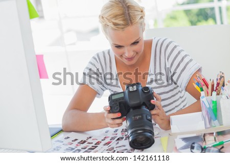 Blonde photo editor looking at a digital camera in her office