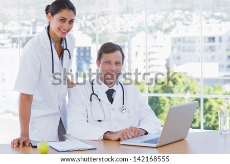 Smiling doctors posing together in their office while working on a laptop
