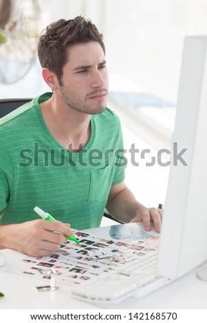 Photo editor working on computer and a contact sheet while holding a green marker