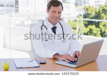 Smiling doctor working on a laptop on his desk