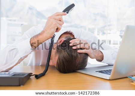 Irritated businessman holding the phone while he is leaning on his desk