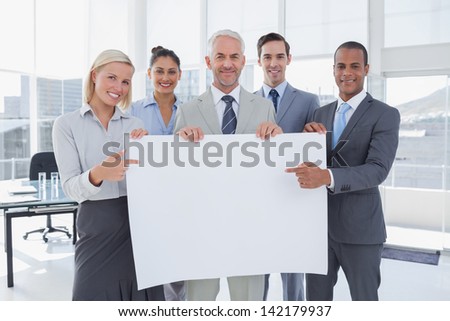 Business team holding large blank poster and pointing to it at the office