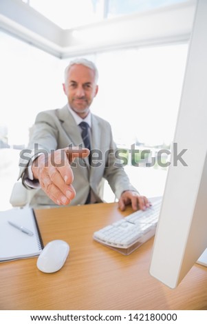 Cheerful businessman reaching hand out for handshake at his desk