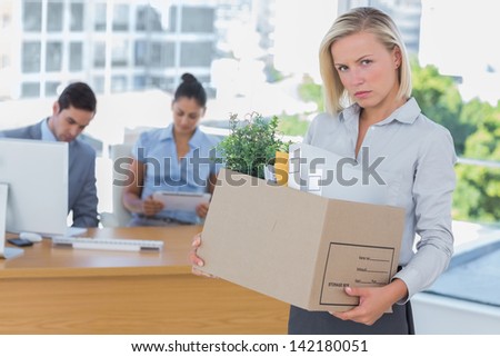 Upset businesswoman leaving office after being let go carrying cardboard box