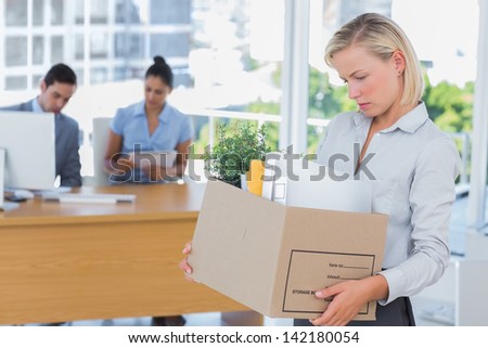 Businesswoman leaving office after being laid off carrying box of belongings