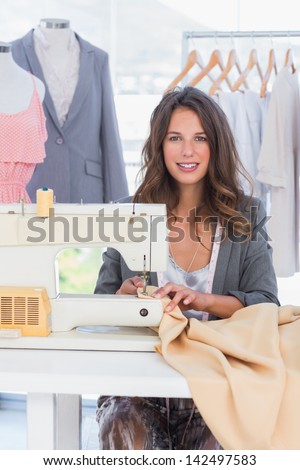 Fashion designer sewing textile and smiling to the camera