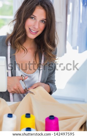 Fashion designer cutting textile next to a sewing machine and smiling to the camera