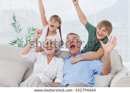 Grandparents and grandchildren raising arms in the living room