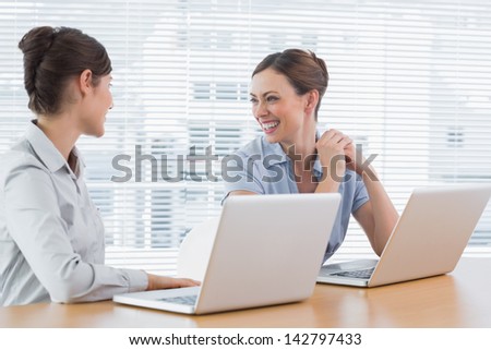 Businesswoman laughing together at desk with laptops in office