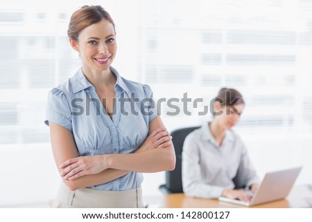 Smiling businesswoman with arms crossed with co worker working behind