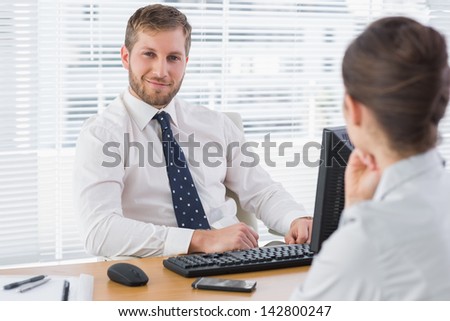 Businessman sitting with a co worker at his desk smiling at the camera