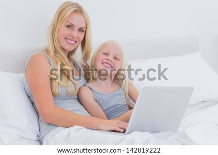 Mother and daughter using a laptop together in bed