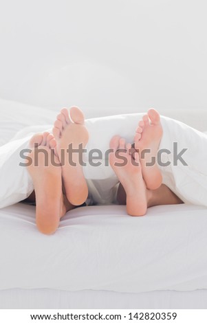 Couple crossing their feet under the duvet in bed