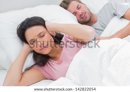 Woman covering ears while her husband is snoring next to her