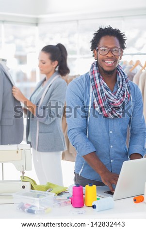 Fashion designer smiling at camera while his colleague adjusting blazer behind him