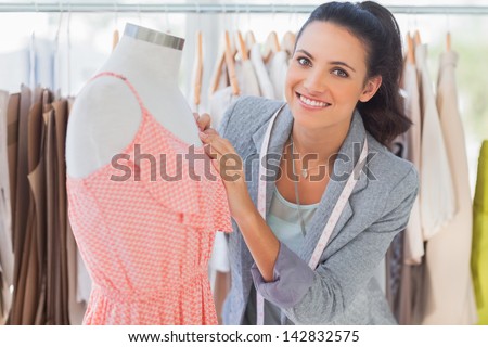 Smiling fashion designer fixing dress on a mannequin in a studio