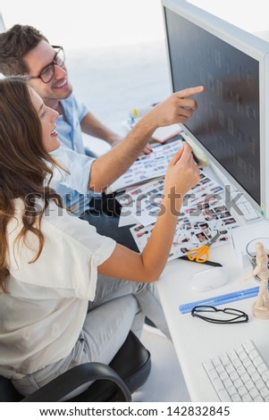 Attractive photo editors pointing at computer with contact sheets on the desk