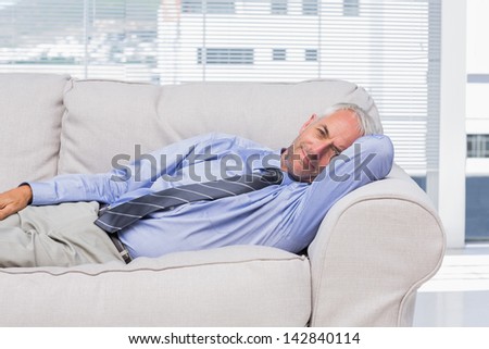 Businessman lying on sofa resting and smiling at camera in office