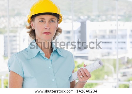 Serious architect looking at camera with helmet and blueprint