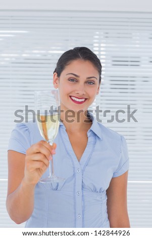 Brunette businesswoman raising a flute of champagne in her office