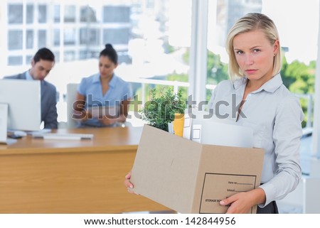 Businesswoman leaving office after being laid off and looking at camera carrying box