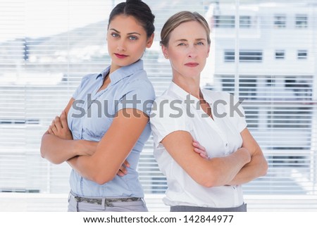 Stern businesswomen standing back to back with arms crossed