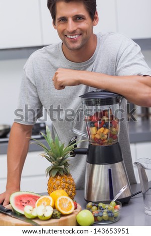Attractive man leaning on his blender with several fruits inside