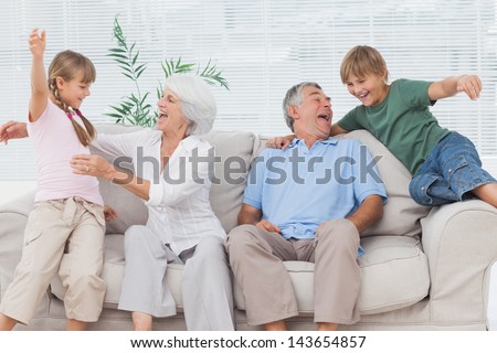 Grandchildren Jumping On Couch With Their Grandparents In The Living Room