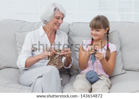 Granddaughter learning how to knit with grandmother sitting on the couch