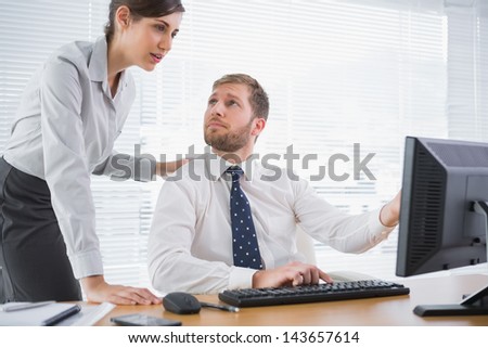 Businessman showing his co worker something on computer at his desk in office