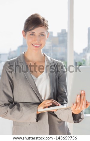 Pretty businesswoman working on laptop and smiling at camera in bright office