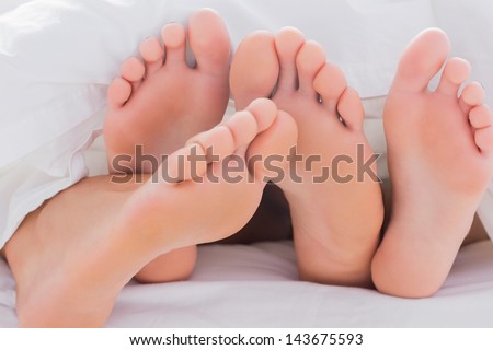 Couple touching their feet together under the duvet in bed