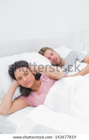 Woman covering her ears while her husband is snoring next to her