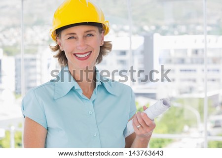 Smiling architect looking at camera with helmet and blueprint