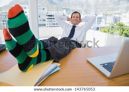 Smiling businessman having a nap with feet over a pile of documents on the desk