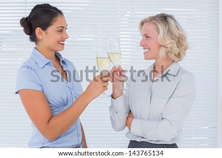 Two cheerful colleagues clinking their flutes of champagne at work