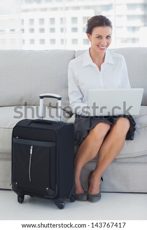 Businesswoman sitting on the couch with laptop with suitcase