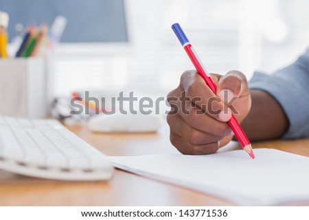 Man drawing with a red pencil on a desk besides a keyboard