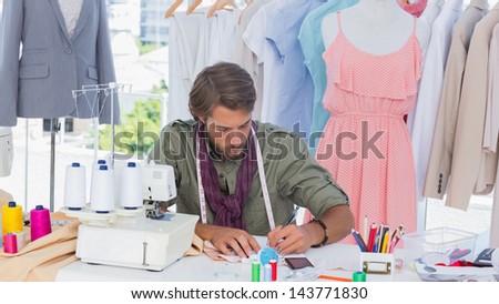 Fashion designer drawing on a desk in front of clothes