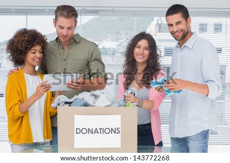 Smiling volunteers using tablet and taking out clothes from donations for a charity