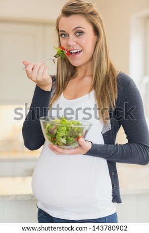 Pregnant woman eating fresh salad bowl in kitchen