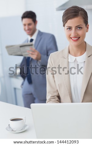 Businesswoman using a laptop before going to work while her husband is reading a newspaper on the background
