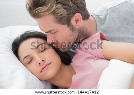 Man kissing his sleeping wife on the cheek in bed