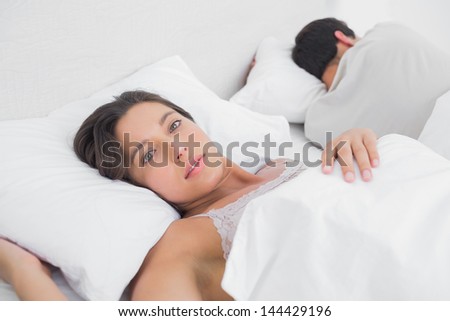 Thoughtful woman sleeping in bed next to her partner