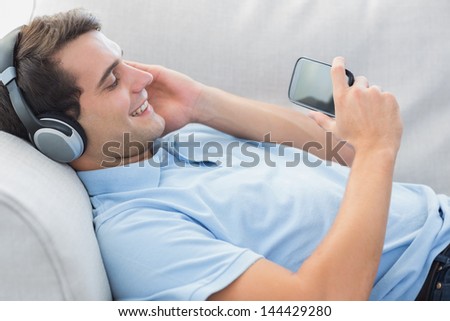 Cheerful man enjoying music with his smartphone laid on a couch