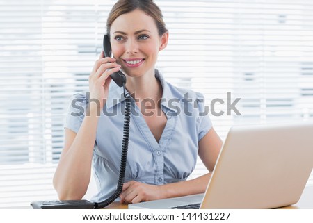 Businesswoman calling and looking away at desk with laptop