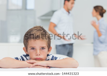 Sad Boy With Arms Folded While Parents Quarreling In The Kitchen